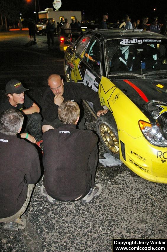 Andy Pinker and members of the SYMS crew assess the right-front suspension of the Tanner Foust/ Chrissie Beavis Subaru WRX STi.