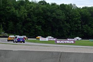 The field follows the pace car through the carousel during an early yellow.