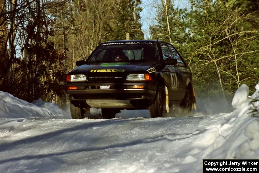 Tom Ottey / Pam McGarvey Mazda 323GTX come over a crest at speed just before sundown.