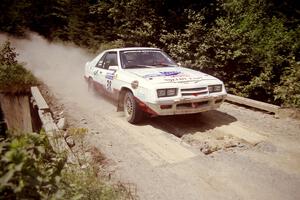 Lesley Suddard / Marc Goldfarb  Dodge Shelby Charger at speed over a bridge on SS5, Magalloway North.