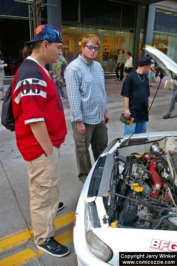 Ben Slocum explains rally to onlookers in front of the Kenny Bartram / Dennis Hotson Subaru Impreza L Coupe.