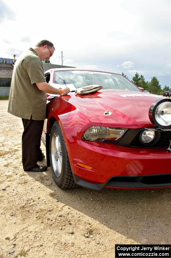 Navigator Rob Bohn reviews notes on the hood of the Ford Mustang driven by Mark Utecht.
