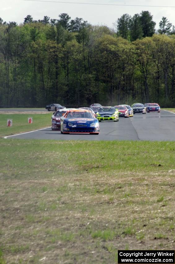 Derek Thorn's Ford Fusion leads the field into turn 4 on lap one.