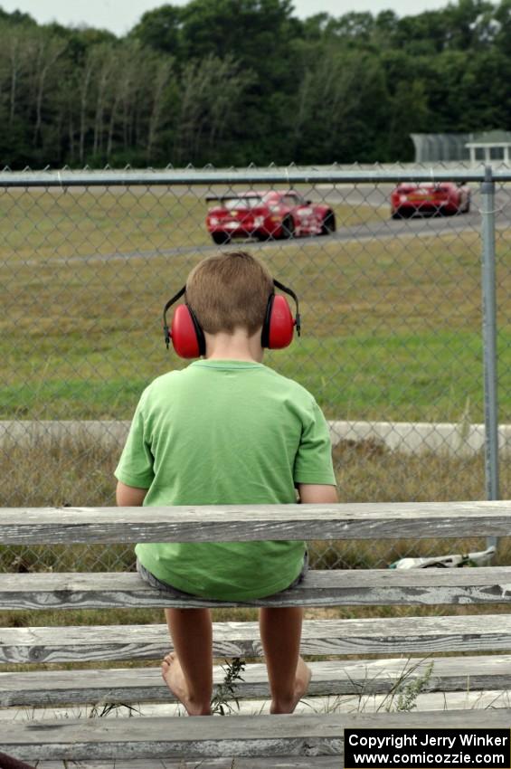 Pete Halsmer's Chevy Camaro chases Bob Stretch's Chevy Camaro as a young fan watches at turn 4.