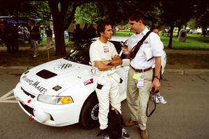 Érik Comas is interviewed by Jeff Burmeister in front of the Mitsubishi Lancer Evo IV he and Julian Masters shared.