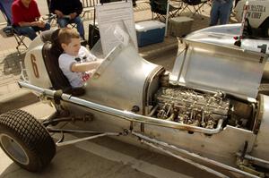 A spectator fits into an old midget racer on display.