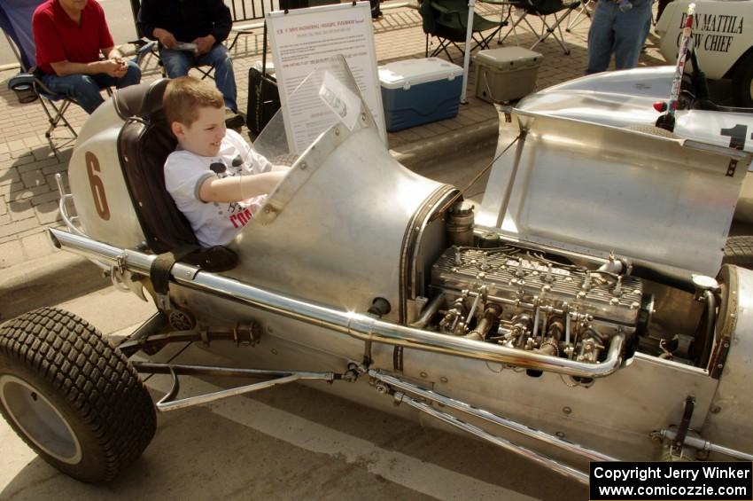 A spectator fits into an old midget racer on display.