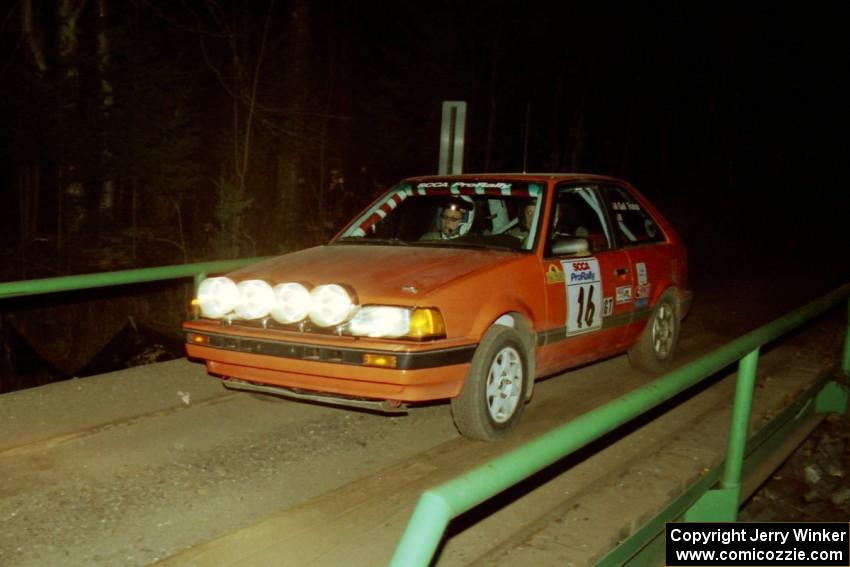 Gail Truess / Pattie Hughes Mazda 323GTX at speed across the final bridge on SS10, Menge Creek.