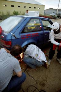 The Darek Bosek / Piotr Modrzejewski Mazda 323GTX receives repairs at service after driving with a flat on a stage.