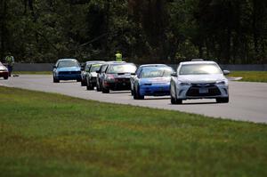 The field follows the pace car out of turn 3 under the yellow flag.