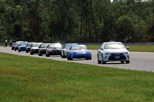 The field follows the pace car out of turn 3 under the yellow flag.