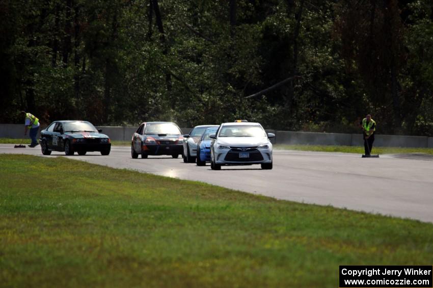 The field follows the pace car out of turn 3 under the yellow flag.