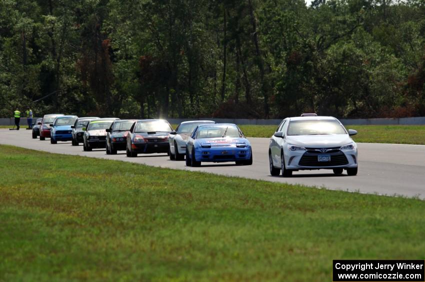 The field follows the pace car out of turn 3 under the yellow flag.