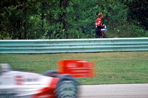 Eddie Cheever walks back to the pits as Emerson Fittipaldi's Penske PC-21/Chevy passes by.