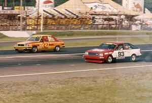 Bobby Archer's Renault Alliance and Dave Frellson's Nissan Sentra go side-by-side down the front straight.