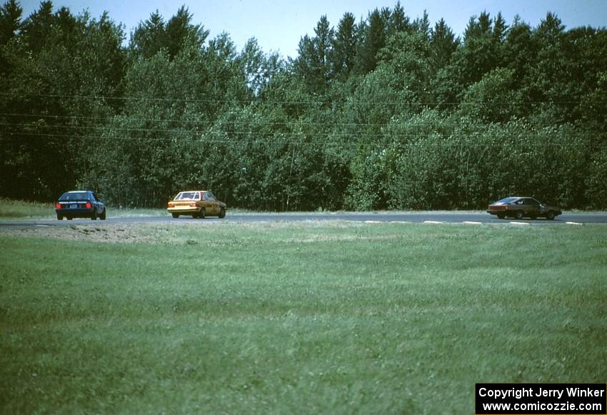 Craig Ross's Datsun 200SX leads Bobby Archer's Renault Alliance and Joe Varde's Dodge Charger through turn 5.