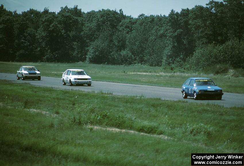 Chuck Ulinski's Mazda 323 leads Joe Nonnamaker's Nissan Stanza and Doug Peterson's Renault Alliance into turn 4.