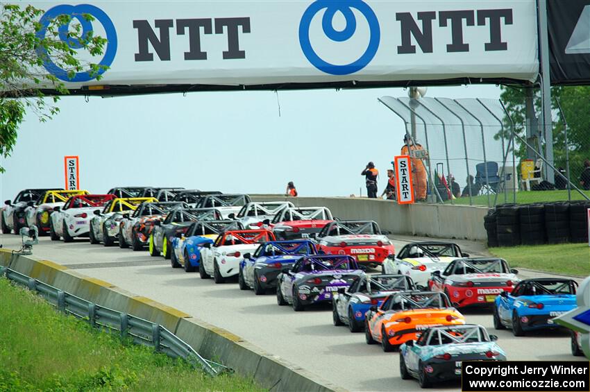 The field of Mazda MX-5 Cup cars head uphill to the green flag.