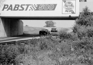 Jack Buchinger's Datsun 280ZX and Rick Anderson's Chevy Corvette pass under the turn 13 bridge.
