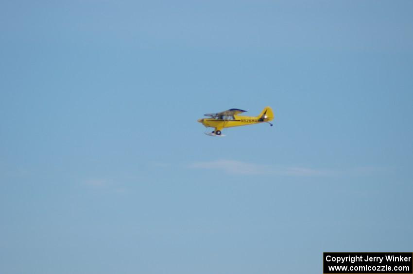 A Piper Cub flies over the track