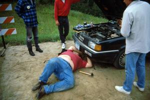 Spectator marshal Norm Johnson struggles to repair the failed alternator belt on his Audi Quattro.