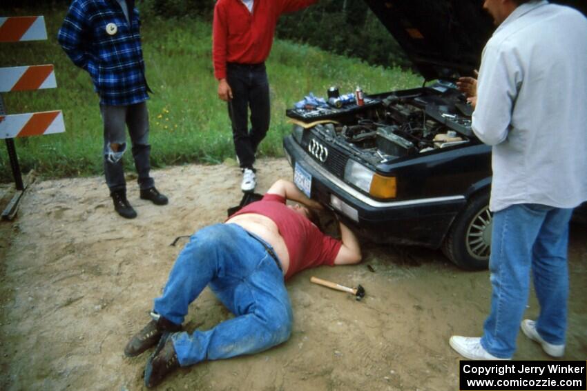 Spectator marshal Norm Johnson struggles to repair the failed alternator belt on his Audi Quattro.