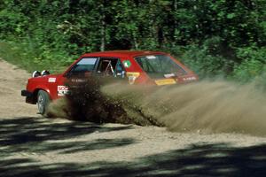 Bill Bjorklund / Al Kintigh kick up a spray of gravel at the crossroads in their Dodge Omni.