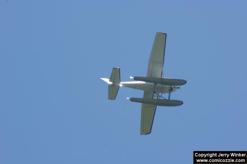 A plane takes off from a nearby lake and circles the track.