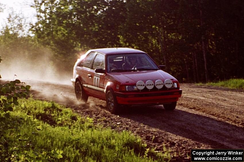 Gail Truess / Pattie Hughes Mazda 323GTX comes by at speed over the crest at the crossroads.